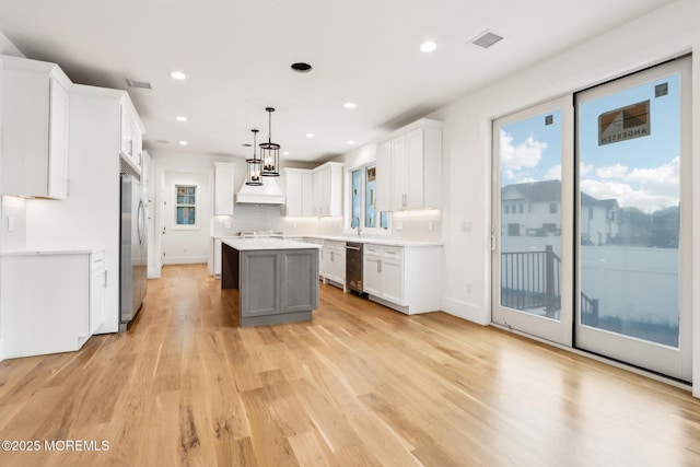 kitchen featuring built in refrigerator, a center island, light wood finished floors, light countertops, and custom range hood