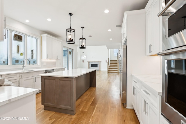 kitchen featuring a kitchen island, a fireplace, light wood-style flooring, a sink, and open floor plan