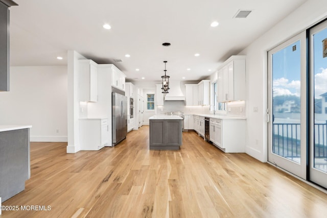 kitchen with built in fridge, custom range hood, a center island, light wood-style floors, and baseboards