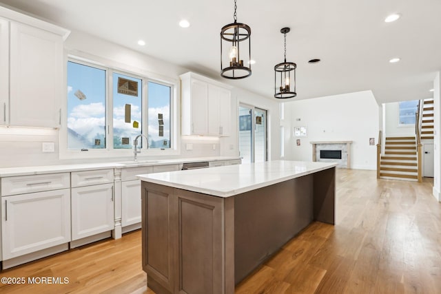 kitchen featuring a fireplace, a sink, open floor plan, a kitchen island, and white cabinets