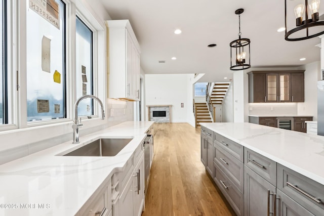 kitchen with a sink, beverage cooler, light wood finished floors, gray cabinetry, and light stone countertops