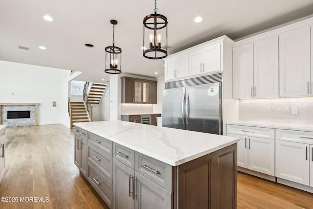 kitchen with built in refrigerator, a glass covered fireplace, open floor plan, backsplash, and white cabinets