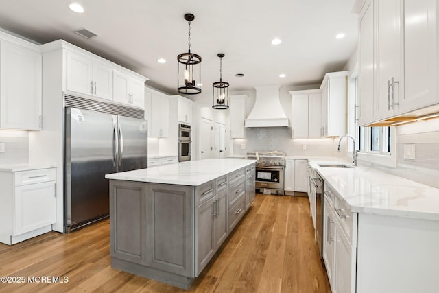 kitchen featuring appliances with stainless steel finishes, premium range hood, a sink, gray cabinets, and a center island