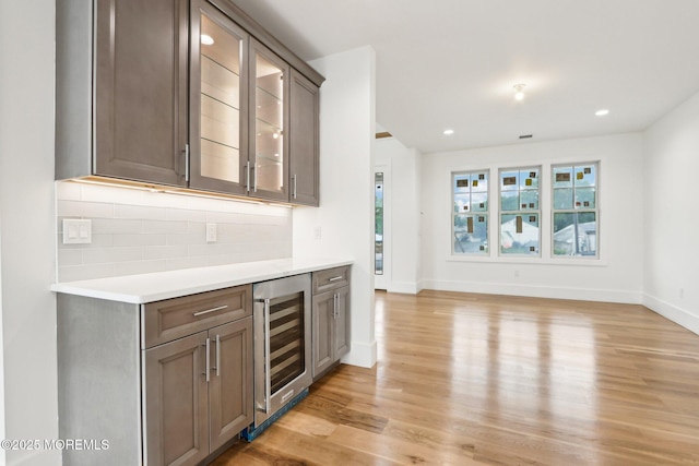indoor dry bar featuring beverage cooler, decorative backsplash, light wood-style floors, baseboards, and recessed lighting
