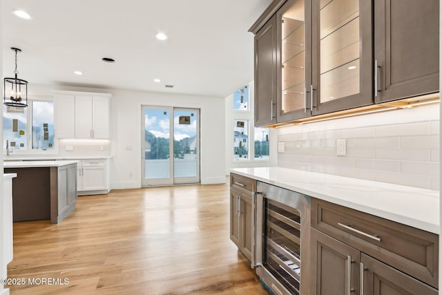 kitchen with beverage cooler, tasteful backsplash, glass insert cabinets, pendant lighting, and light wood-type flooring