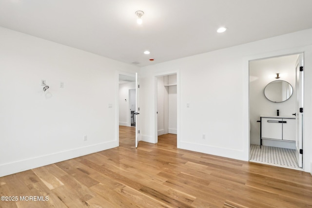 unfurnished bedroom featuring baseboards, light wood-style flooring, recessed lighting, connected bathroom, and a walk in closet