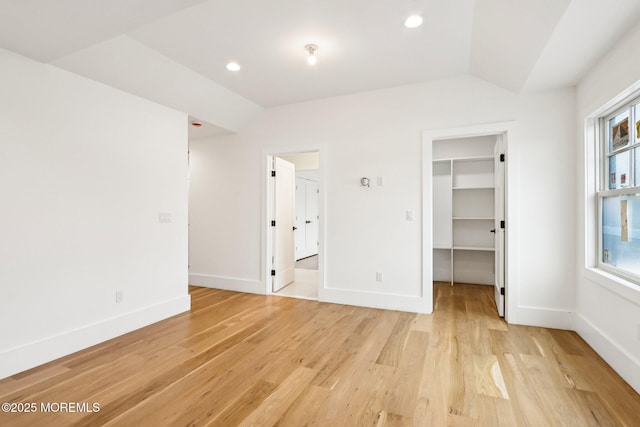 unfurnished bedroom featuring light wood-style floors, a spacious closet, baseboards, recessed lighting, and vaulted ceiling