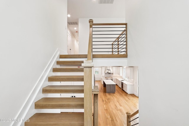 staircase with a high ceiling, wood finished floors, and recessed lighting