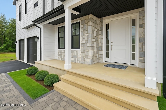 property entrance with covered porch, stone siding, a garage, and asphalt driveway