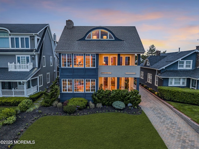 2009 Ocean Ave, Spring Lake, NJ 07762 - back of house at dusk featuring a yard, a chimney, a shingled roof, and decorative driveway