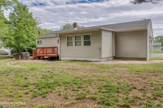 rear view of house with a chimney, a wooden deck, and a lawn