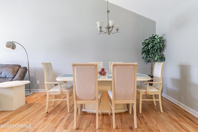 dining space with light wood finished floors, a chandelier, lofted ceiling, and baseboards