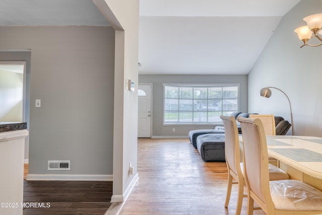 hall with wood finished floors, lofted ceiling, baseboards, and a chandelier