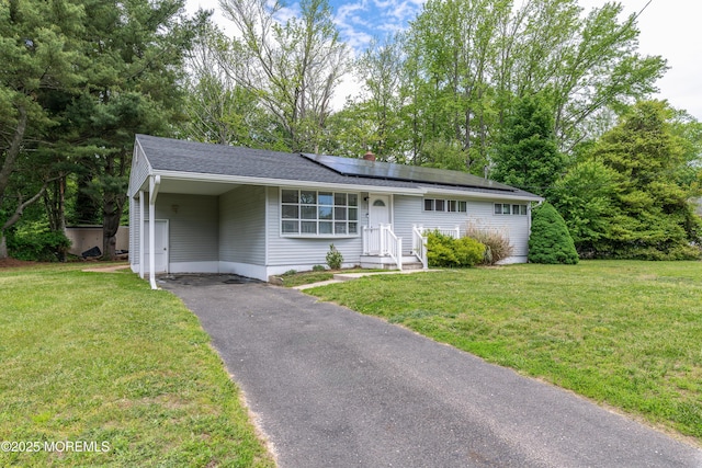ranch-style house with asphalt driveway, roof mounted solar panels, a front lawn, and a carport
