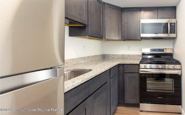kitchen featuring appliances with stainless steel finishes, light stone counters, light wood finished floors, and dark brown cabinets