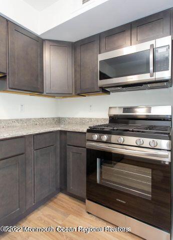kitchen with appliances with stainless steel finishes, light wood-type flooring, dark brown cabinetry, and light stone counters