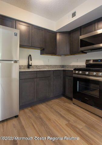 kitchen featuring stainless steel appliances, light wood-style flooring, dark brown cabinets, a textured ceiling, and a sink