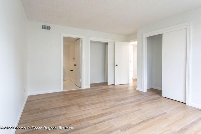 unfurnished bedroom featuring light wood-type flooring, two closets, ensuite bath, and baseboards