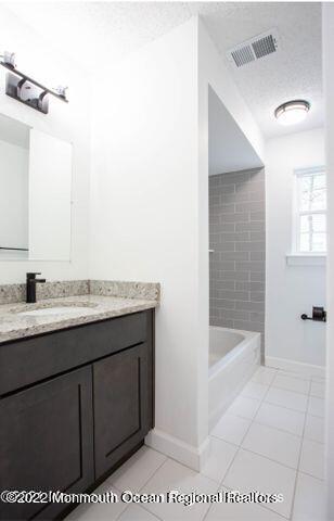 full bath with tile patterned flooring, vanity, a textured ceiling, and baseboards