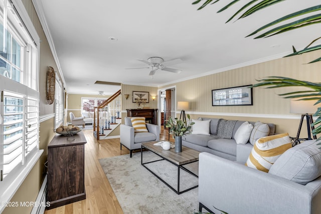 living room with stairway, ornamental molding, wood finished floors, a ceiling fan, and baseboards