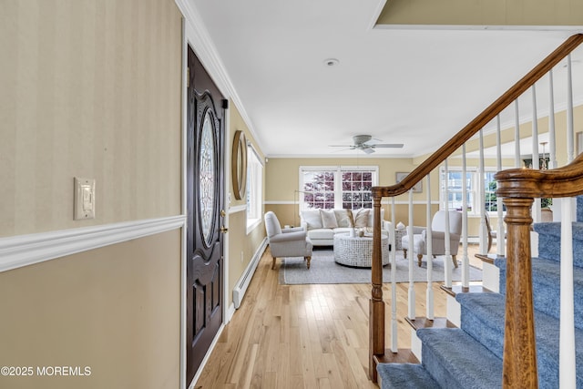 foyer entrance featuring baseboard heating, crown molding, stairs, light wood-style flooring, and baseboards