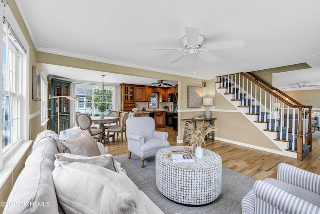 living room with a ceiling fan, light wood-style flooring, stairs, ornamental molding, and baseboards