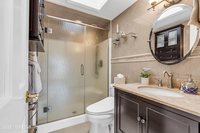 bathroom featuring a shower stall, toilet, vanity, tile walls, and tile patterned floors