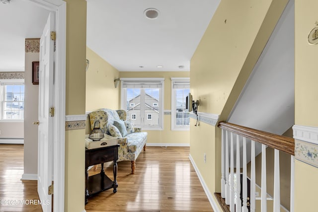 hall featuring baseboard heating, hardwood / wood-style floors, and baseboards