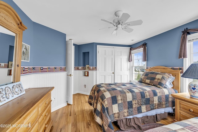 bedroom featuring wainscoting, light wood-type flooring, a closet, ceiling fan, and baseboards