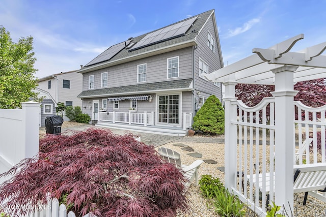 view of front of home with roof with shingles, solar panels, fence, and a pergola