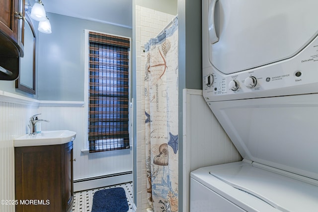 clothes washing area with baseboard heating, estacked washer and dryer, and a wainscoted wall