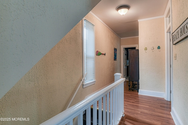 hallway featuring a textured wall, wood finished floors, and ornamental molding