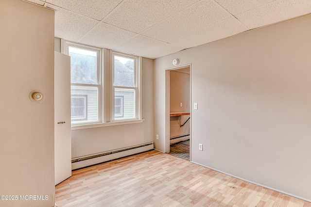 unfurnished room with a baseboard radiator, wood finished floors, a drop ceiling, and a smoke detector