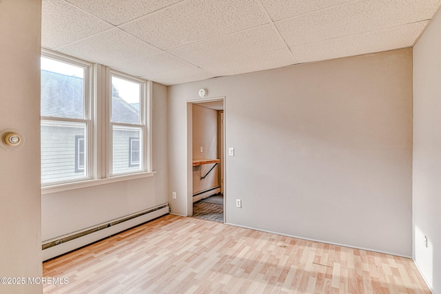 empty room with a baseboard radiator, wood finished floors, and a drop ceiling