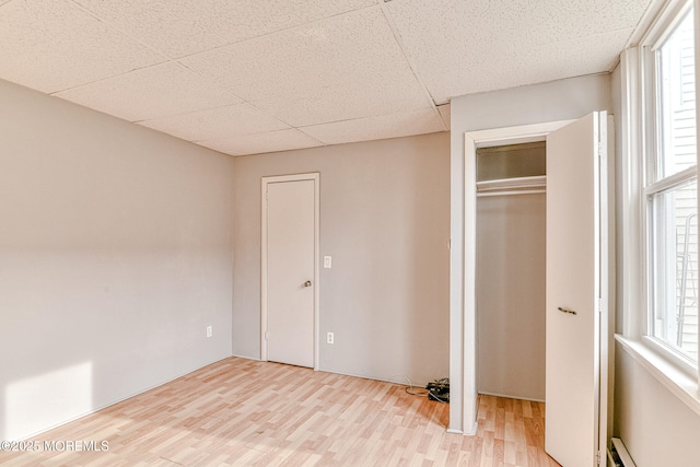 unfurnished bedroom featuring wood finished floors, baseboard heating, a closet, and a drop ceiling