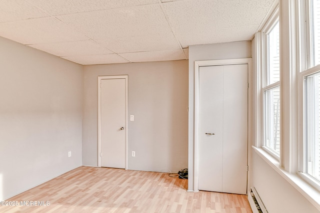 unfurnished bedroom with a baseboard heating unit, wood finished floors, and a closet
