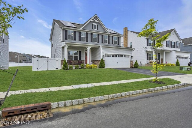83 Weston Dr, Woolwich, NJ 08085 - view of front facade with a gate, roof mounted solar panels, asphalt driveway, stone siding, and board and batten siding