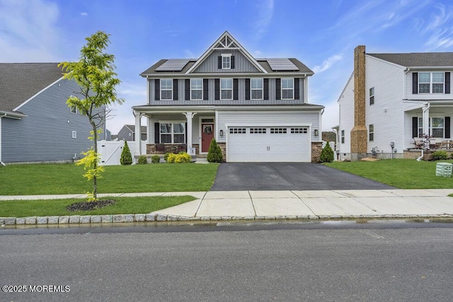 83 Weston Dr, Woolwich, NJ 08085 - view of front of house featuring asphalt driveway, covered porch, an attached garage, roof mounted solar panels, and stone siding