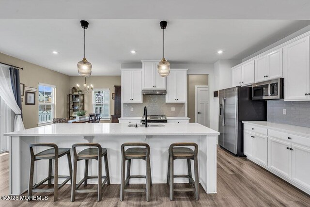 83 Weston Dr, Woolwich, NJ 08085 - kitchen featuring appliances with stainless steel finishes, tasteful backsplash, under cabinet range hood, white cabinets, and a breakfast bar