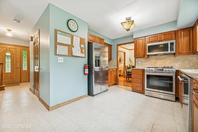 325 Oak Hill Rd, Red Bank, NJ 07701 - kitchen with stainless steel appliances, backsplash, brown cabinetry, light stone countertops, and light tile patterned floors