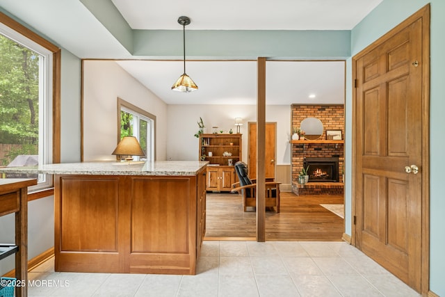 325 Oak Hill Rd, Red Bank, NJ 07701 - kitchen featuring a brick fireplace, decorative light fixtures, light tile patterned flooring, light stone counters, and brown cabinets