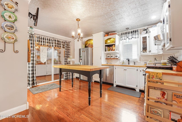 kitchen featuring stainless steel appliances, light wood-style floors, white cabinets, a sink, and a chandelier