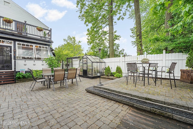 view of patio / terrace with a greenhouse, outdoor dining space, a balcony, and an outbuilding