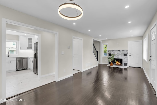 living room with stairs, recessed lighting, a warm lit fireplace, light wood-style floors, and baseboards