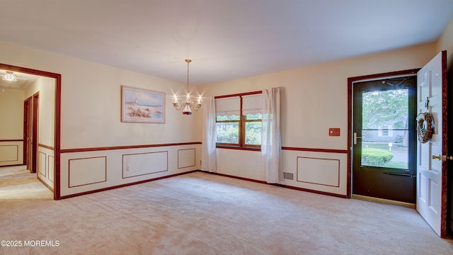 unfurnished room with healthy amount of natural light, a chandelier, carpet flooring, a wainscoted wall, and a decorative wall