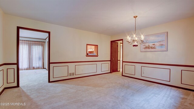 empty room featuring a chandelier, a decorative wall, a wainscoted wall, and light colored carpet