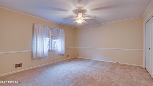 empty room with ceiling fan, light colored carpet, crown molding, and baseboards