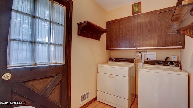 clothes washing area with washer and clothes dryer, cabinet space, and light wood finished floors