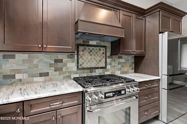 kitchen featuring stainless steel gas range, custom range hood, freestanding refrigerator, and light stone counters