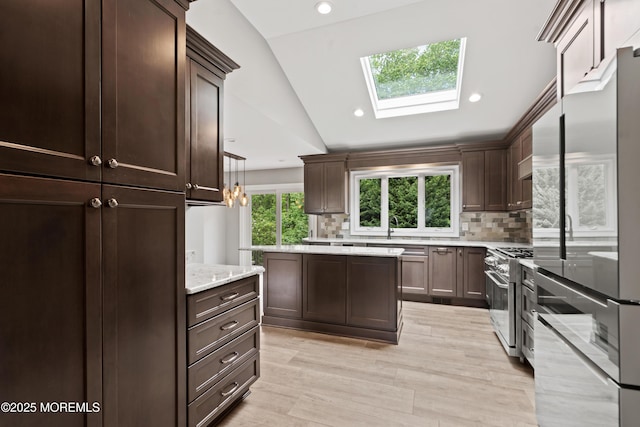 kitchen featuring stainless steel appliances, vaulted ceiling, a skylight, tasteful backsplash, and dark brown cabinetry